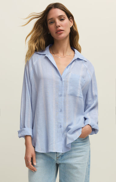 Woman wearing a light blue striped shirt and jeans against a plain background