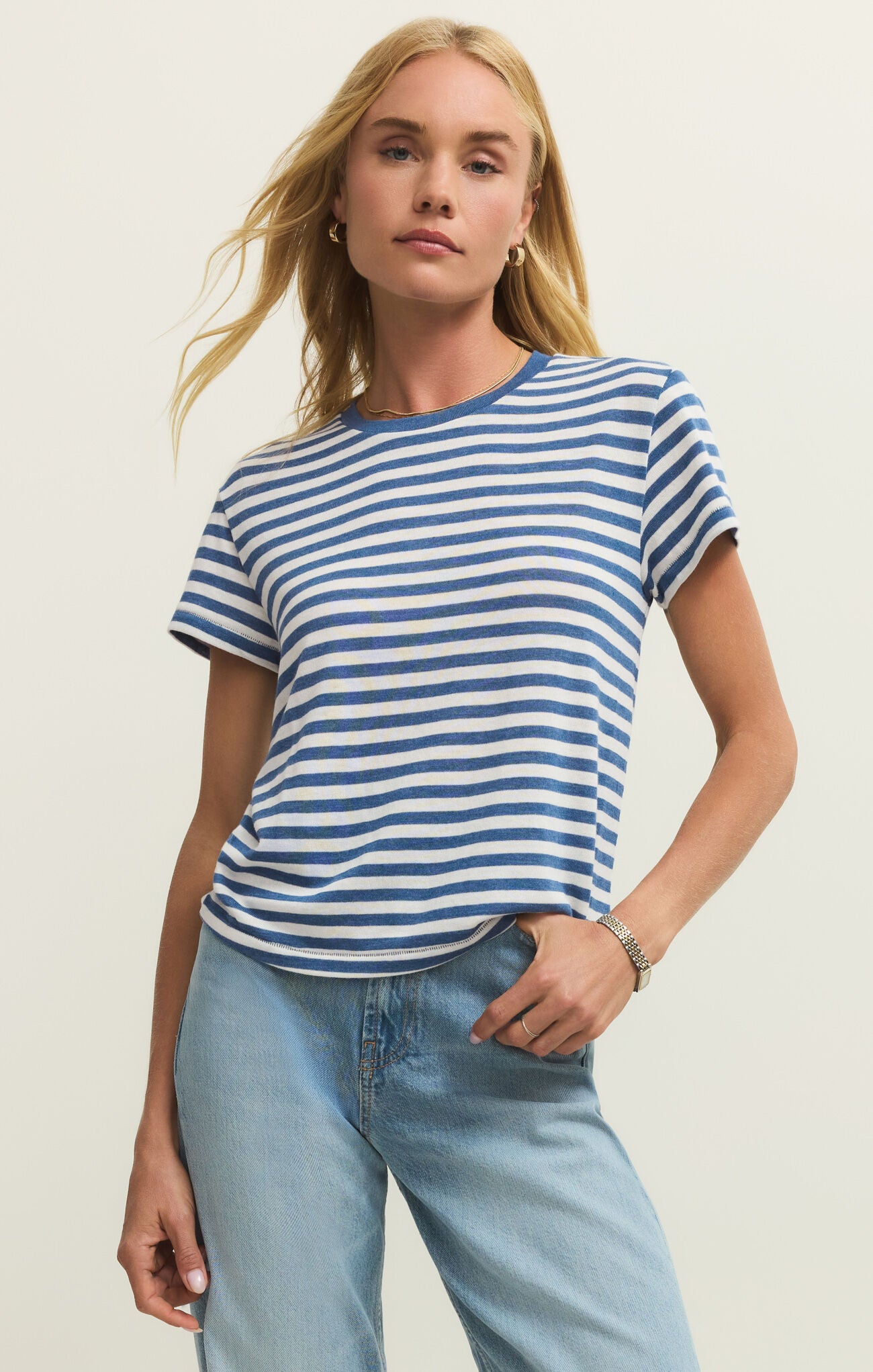 Woman wearing a blue and white striped t-shirt and light blue jeans against a plain background