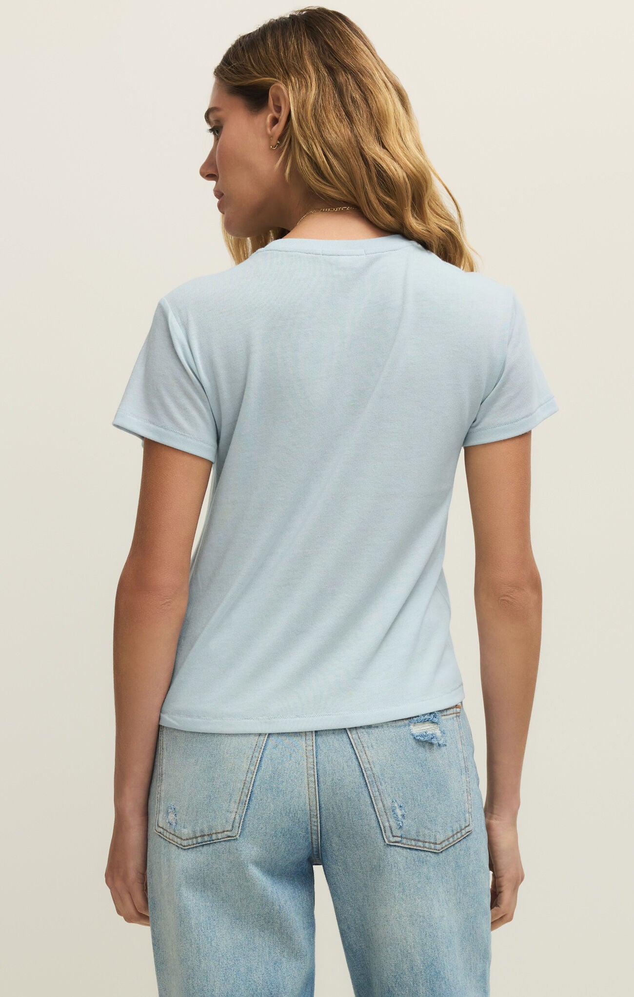 Woman wearing a light blue t-shirt and jeans on a beige background