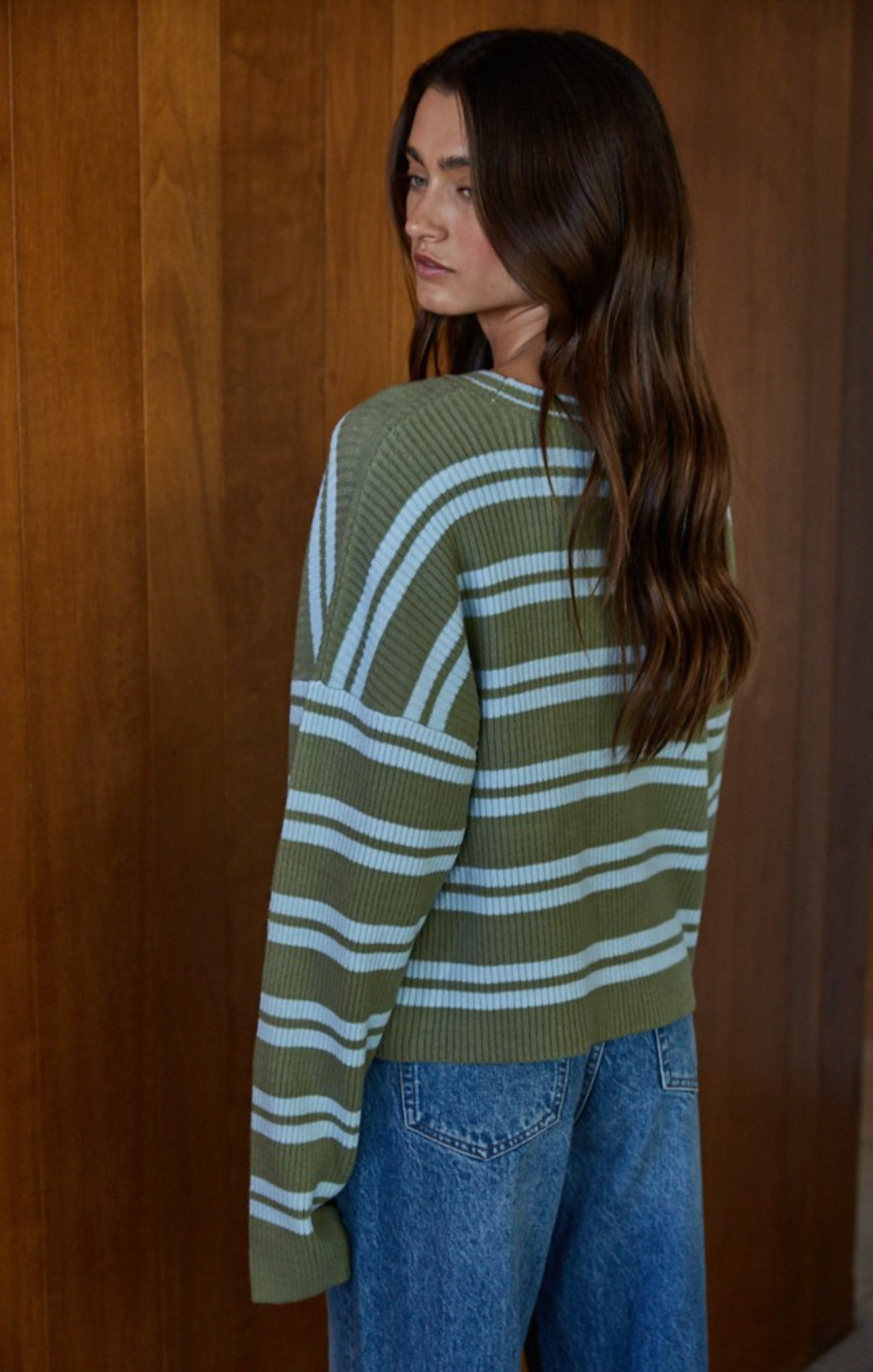Woman wearing a green and white striped sweater against a wooden wall