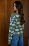 Woman wearing a green and white striped sweater against a wooden wall