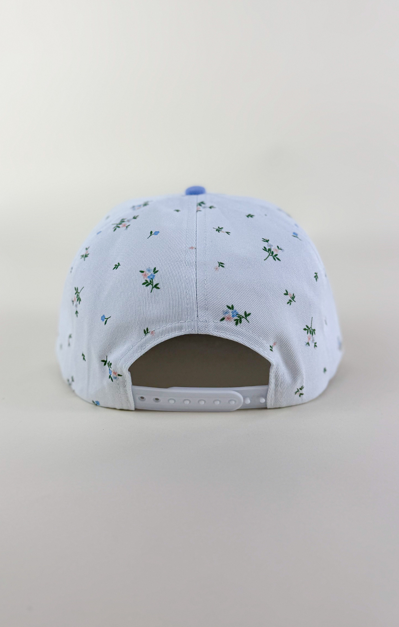 Light blue and white two-tone baseball cap with a solid light blue brim and a white crown featuring a delicate scattered floral print in blue and green.