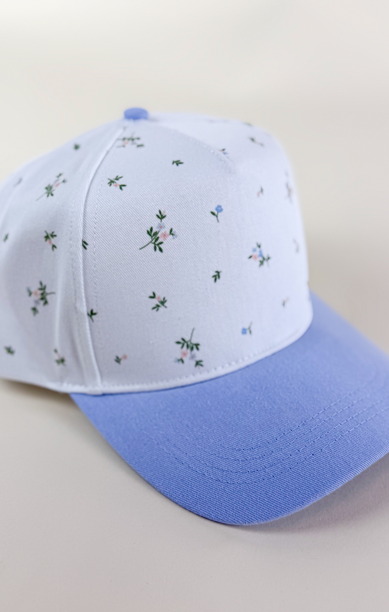 Light blue and white two-tone baseball cap with a solid light blue brim and a white crown featuring a delicate scattered floral print in blue and green.