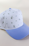 Light blue and white two-tone baseball cap with a solid light blue brim and a white crown featuring a delicate scattered floral print in blue and green.