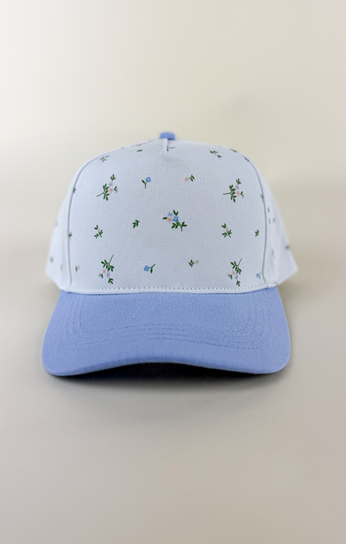 Light blue and white two-tone baseball cap with a solid light blue brim and a white crown featuring a delicate scattered floral print in blue and green.