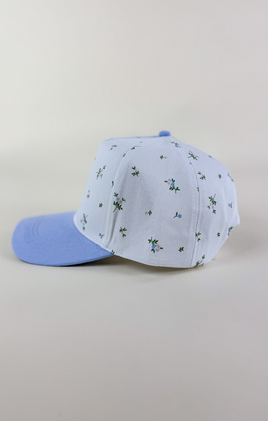 Light blue and white two-tone baseball cap with a solid light blue brim and a white crown featuring a delicate scattered floral print in blue and green.