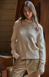 Woman wearing a beige sweater and pants in a warm-toned indoor setting