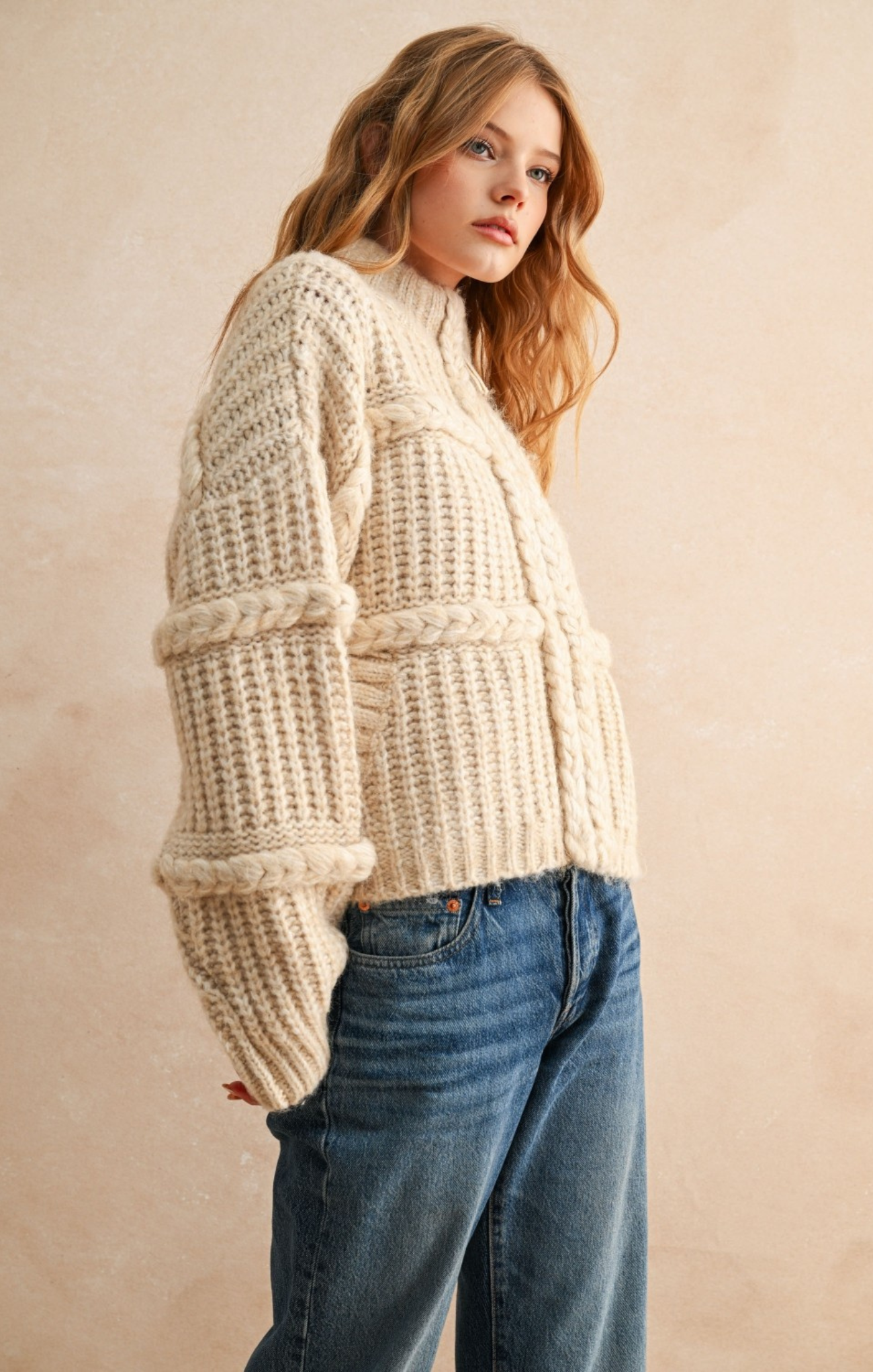 Woman wearing a chunky knit sweater and jeans against a beige background