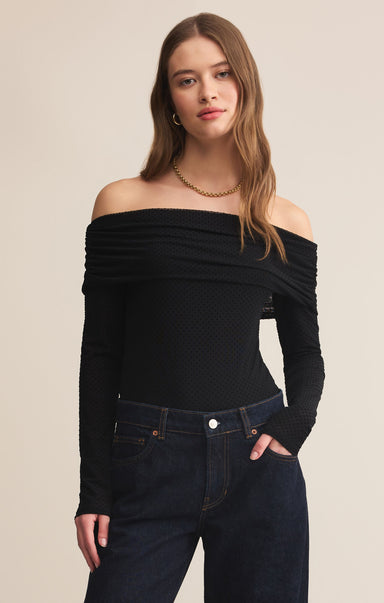 Woman wearing a black off-shoulder top and dark jeans on a beige background