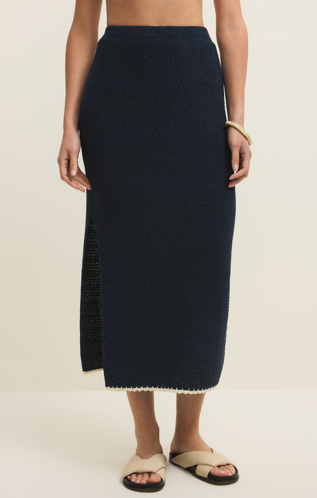 Person wearing a navy blue knit skirt on a beige background