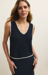 Woman wearing a navy sleeveless top with white trim against a beige background