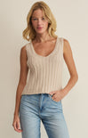 Woman wearing a beige ribbed tank top and blue jeans against a plain background
