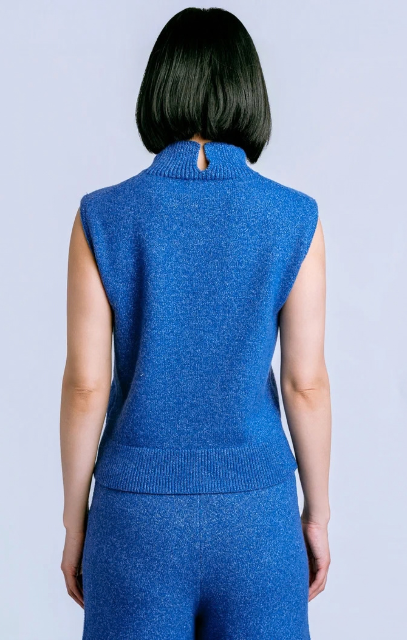 A person shown from the back wearing a sleeveless blue knit mock-neck top and matching blue knit bottoms against a light gray studio background.