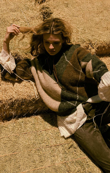 Person wearing a patterned sweater sitting on hay