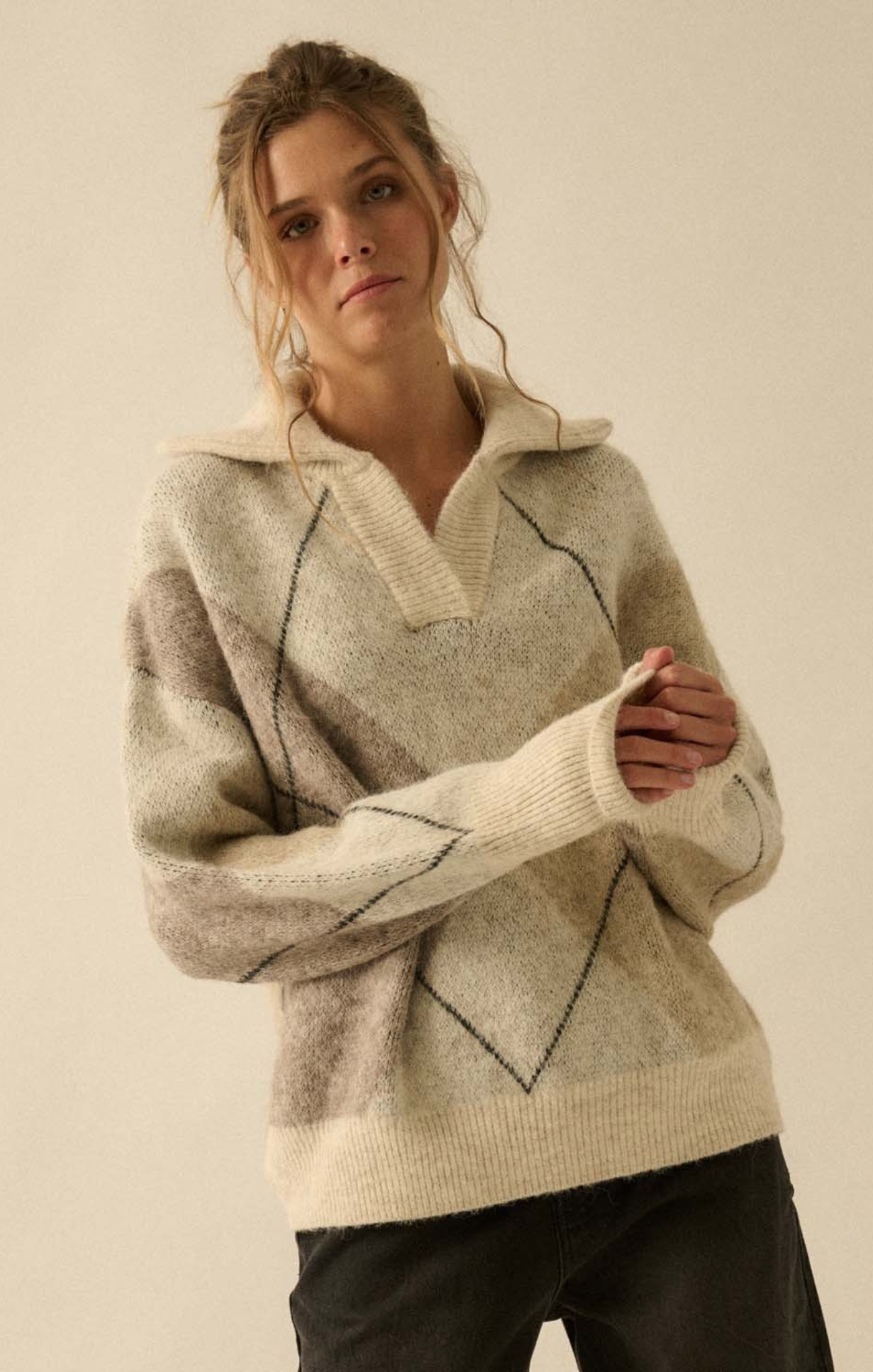 Woman wearing a beige sweater with a subtle pattern on a plain background