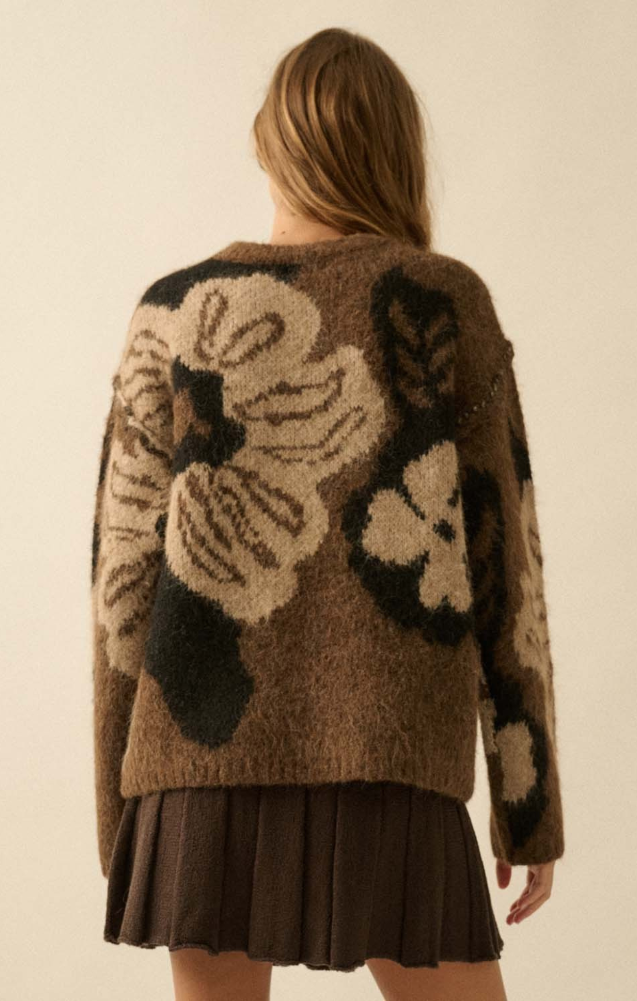 Person wearing a brown floral-patterned sweater against a beige background