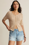 Woman wearing a beige lace cardigan and denim shorts on a plain background