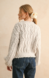 Woman wearing a white cable knit sweater and blue jeans against a beige background