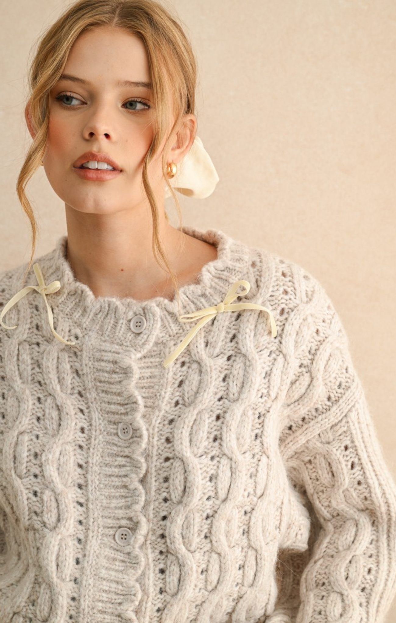 Woman wearing a detailed cable knit sweater against a beige background
