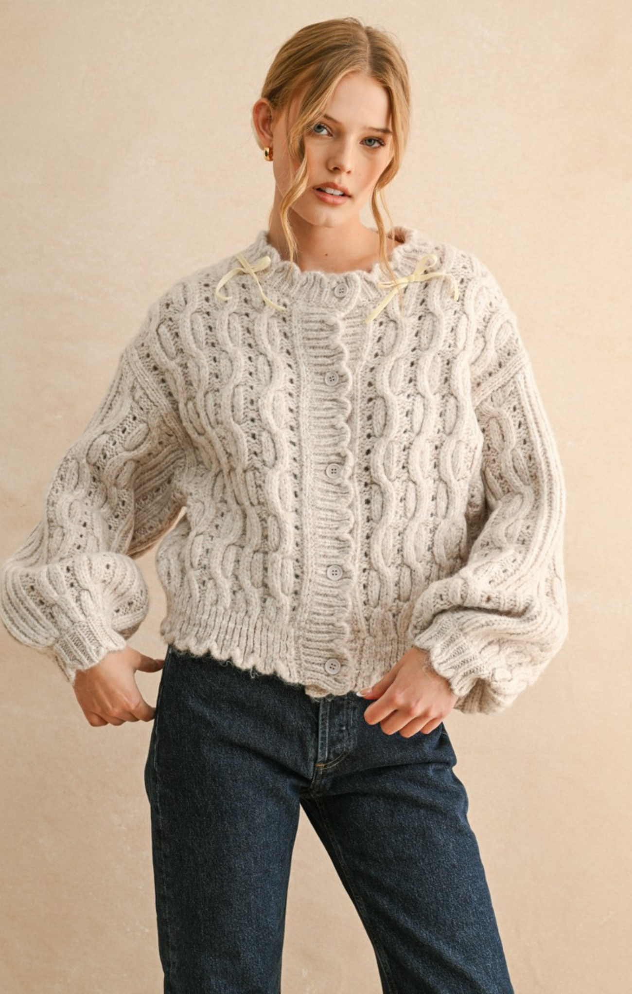 Woman wearing a white knitted sweater and blue jeans on a beige background