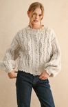 Woman wearing a white knitted sweater and blue jeans on a beige background
