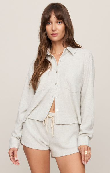 Woman wearing a light gray button-up shirt and shorts on a plain background