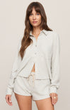 Woman wearing a light gray button-up shirt and shorts on a plain background