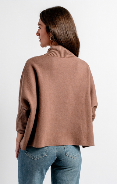 A woman shown from the back wearing a cropped, oversized ribbed knit sweater in a dusty rose-brown color, paired with blue jeans, against a plain white studio background.