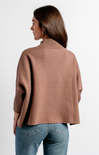 A woman shown from the back wearing a cropped, oversized ribbed knit sweater in a dusty rose-brown color, paired with blue jeans, against a plain white studio background.