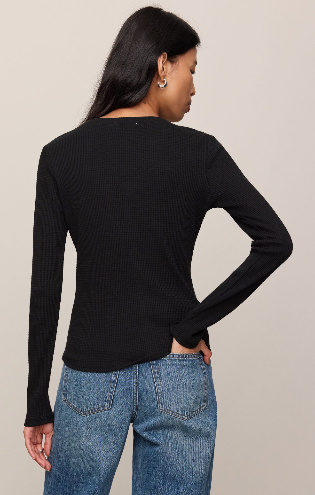 Person wearing a black long-sleeve top and blue jeans on a beige background