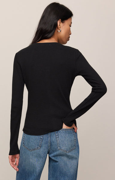 Person wearing a black long-sleeve top and blue jeans on a beige background