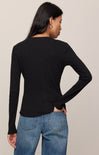 Person wearing a black long-sleeve top and blue jeans on a beige background