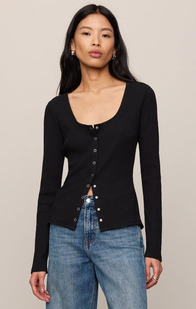 Woman wearing a black cardigan over a blue top against a beige background