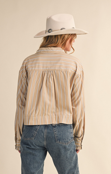 Person wearing a beige striped shirt, blue jeans, and a white hat on a beige background
