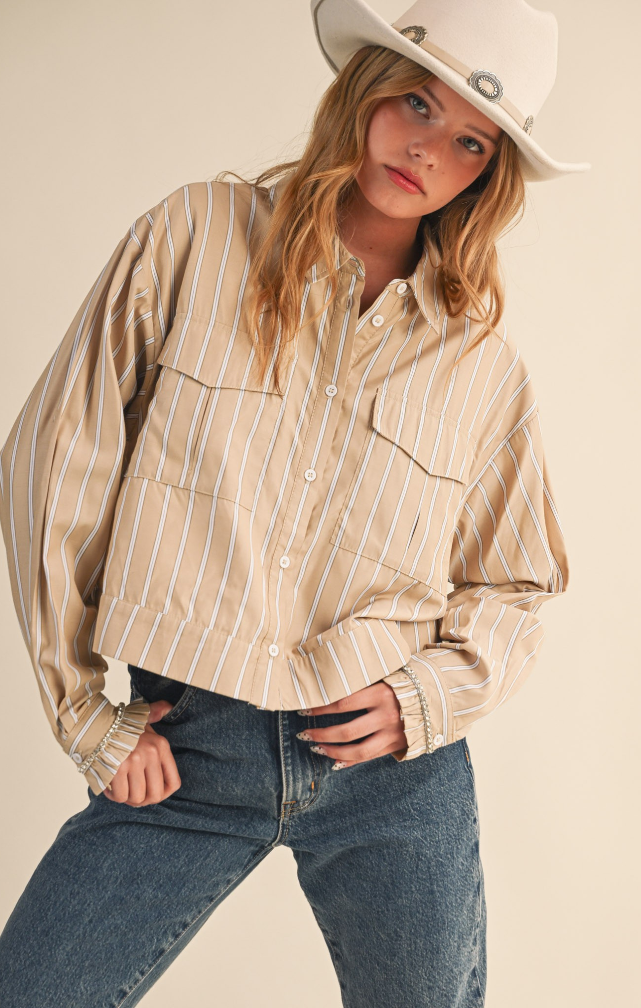 Person wearing a beige striped shirt, blue jeans, and a white cowboy hat on a plain background