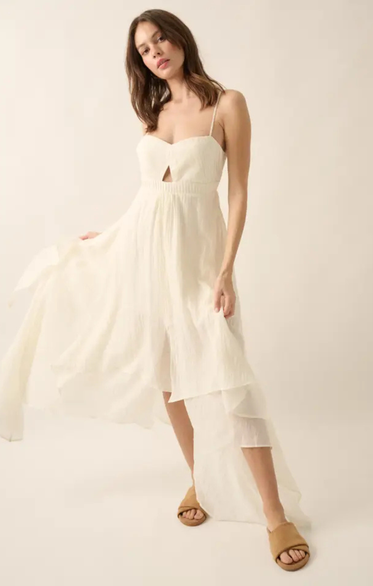 Woman wearing a white dress with a cutout design on a plain background