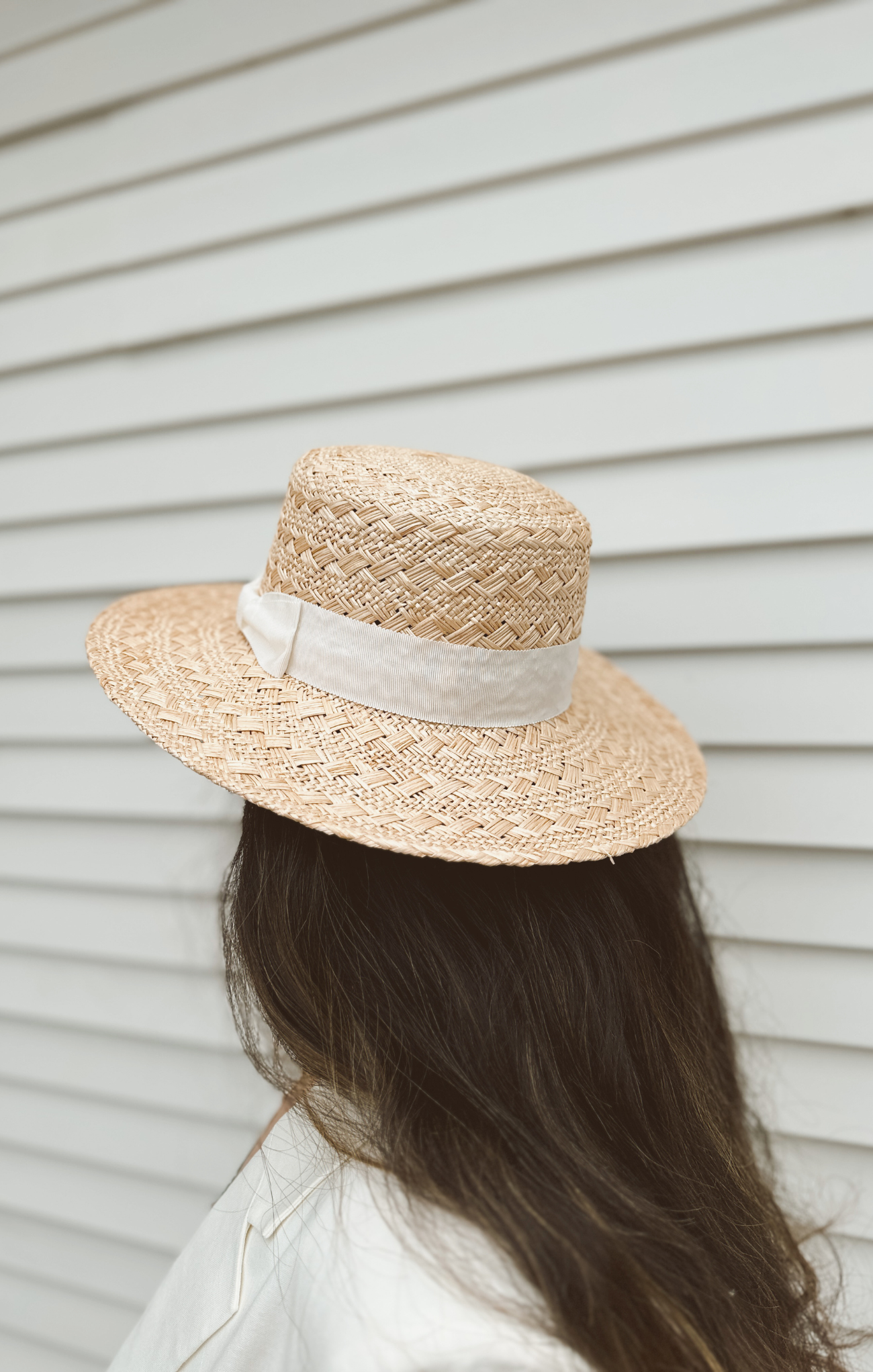 Person wearing a straw hat with a white ribbon against a neutral background