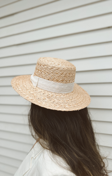 Person wearing a straw hat with a white ribbon against a neutral background