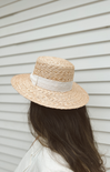 Person wearing a straw hat with a white ribbon against a neutral background