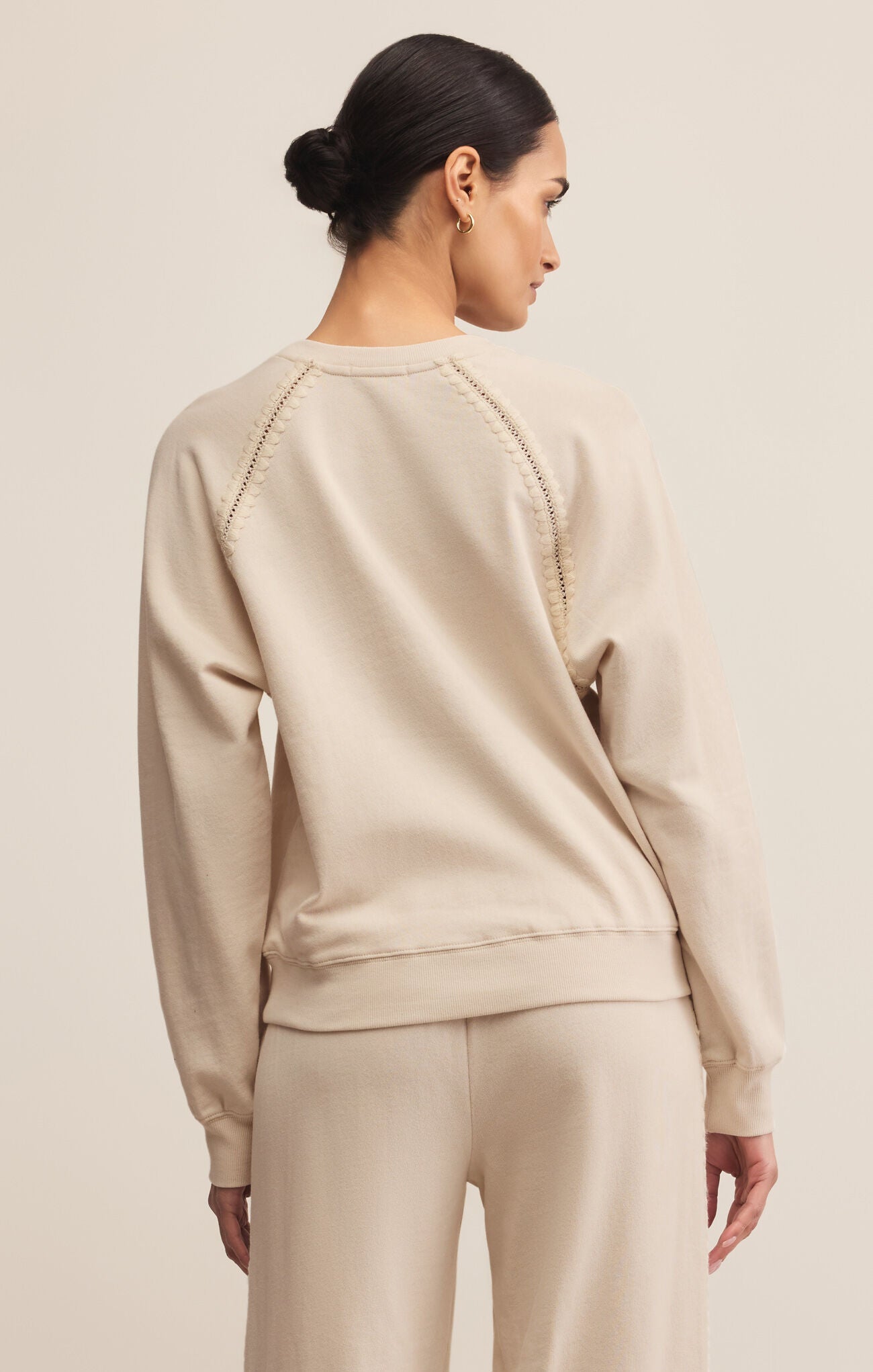 Woman wearing a beige sweatshirt and pants on a plain background