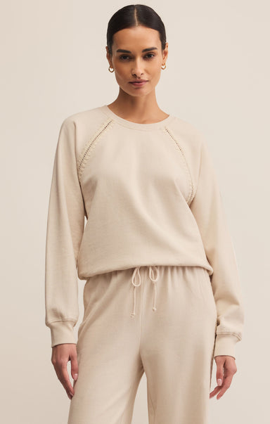 A female model wearing a beige long-sleeve sweatshirt with a crew neck, made of cotton, and matching pants, standing against a plain background.