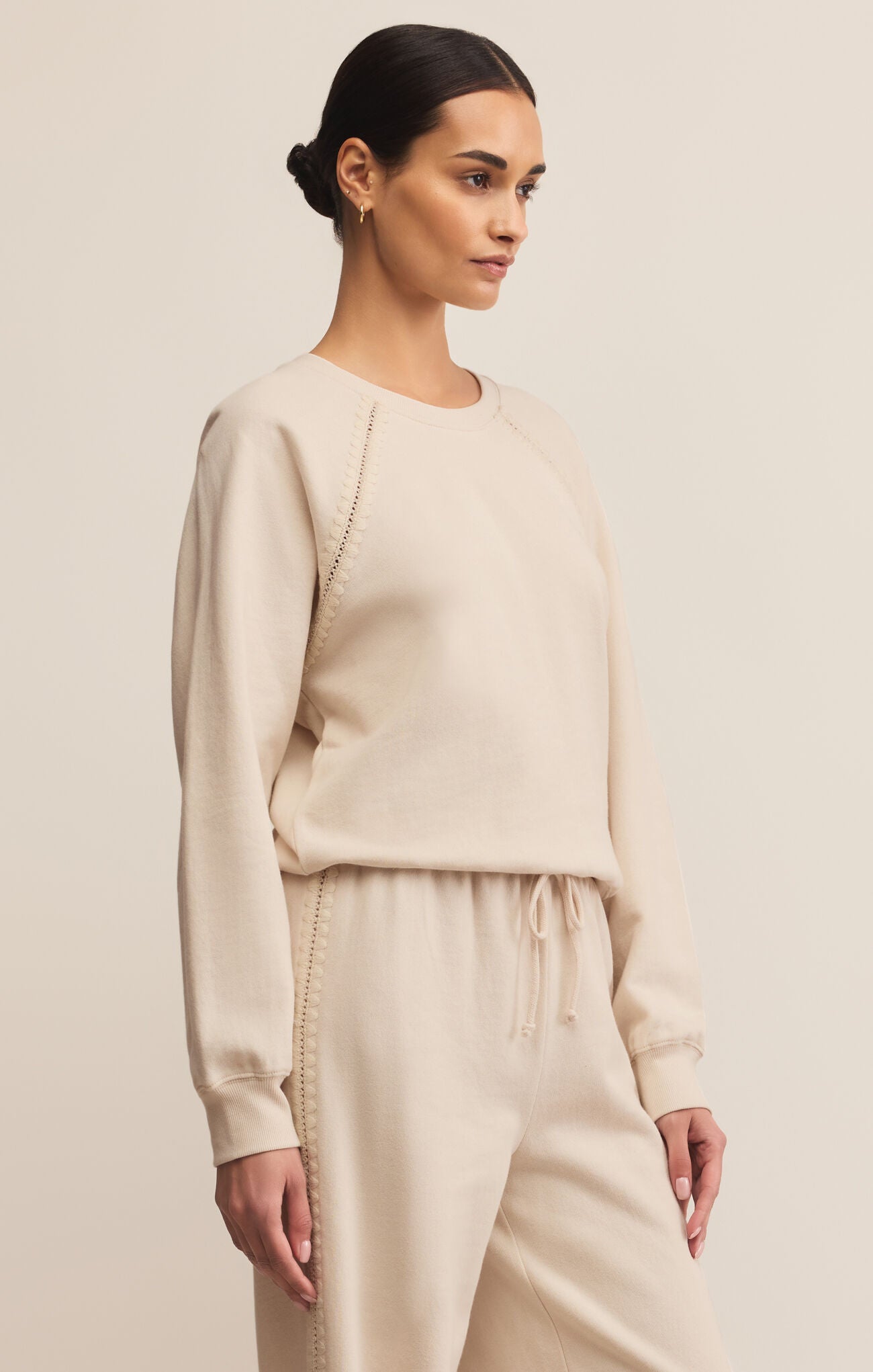 Woman wearing a beige sweater and pants set against a plain background