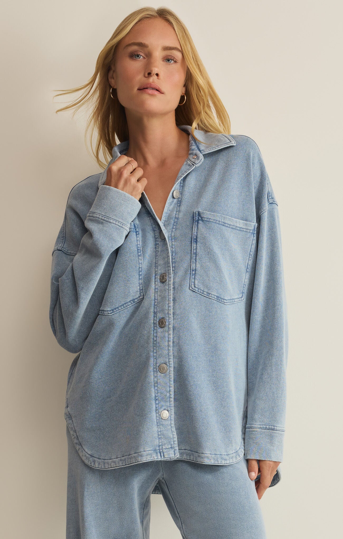 Woman wearing a light blue denim shirt against a beige background