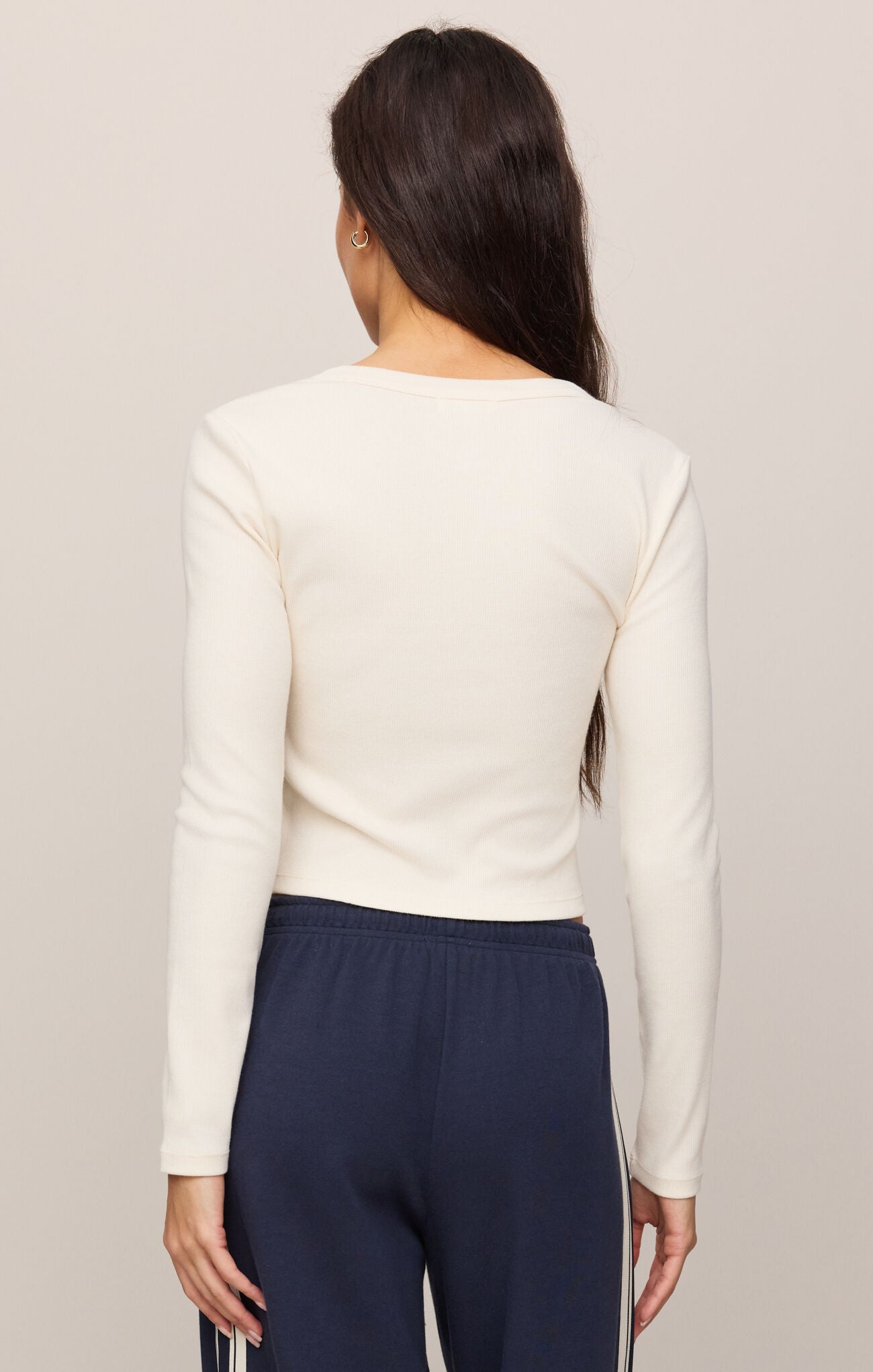 Person wearing a cream long-sleeve top and navy pants against a plain background