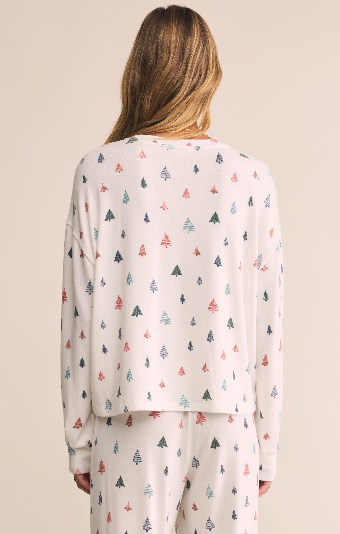 Person wearing a white long-sleeve top and pants with colorful tree pattern on a beige background