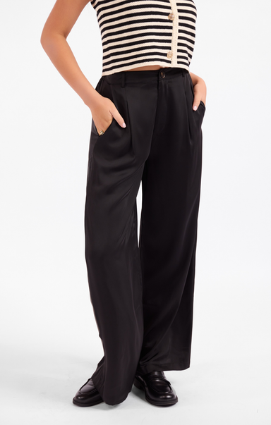 A model wearing black wide-leg trousers with side pockets, paired with a black and white striped top and black loafers, shown from the chest down on a white studio background.