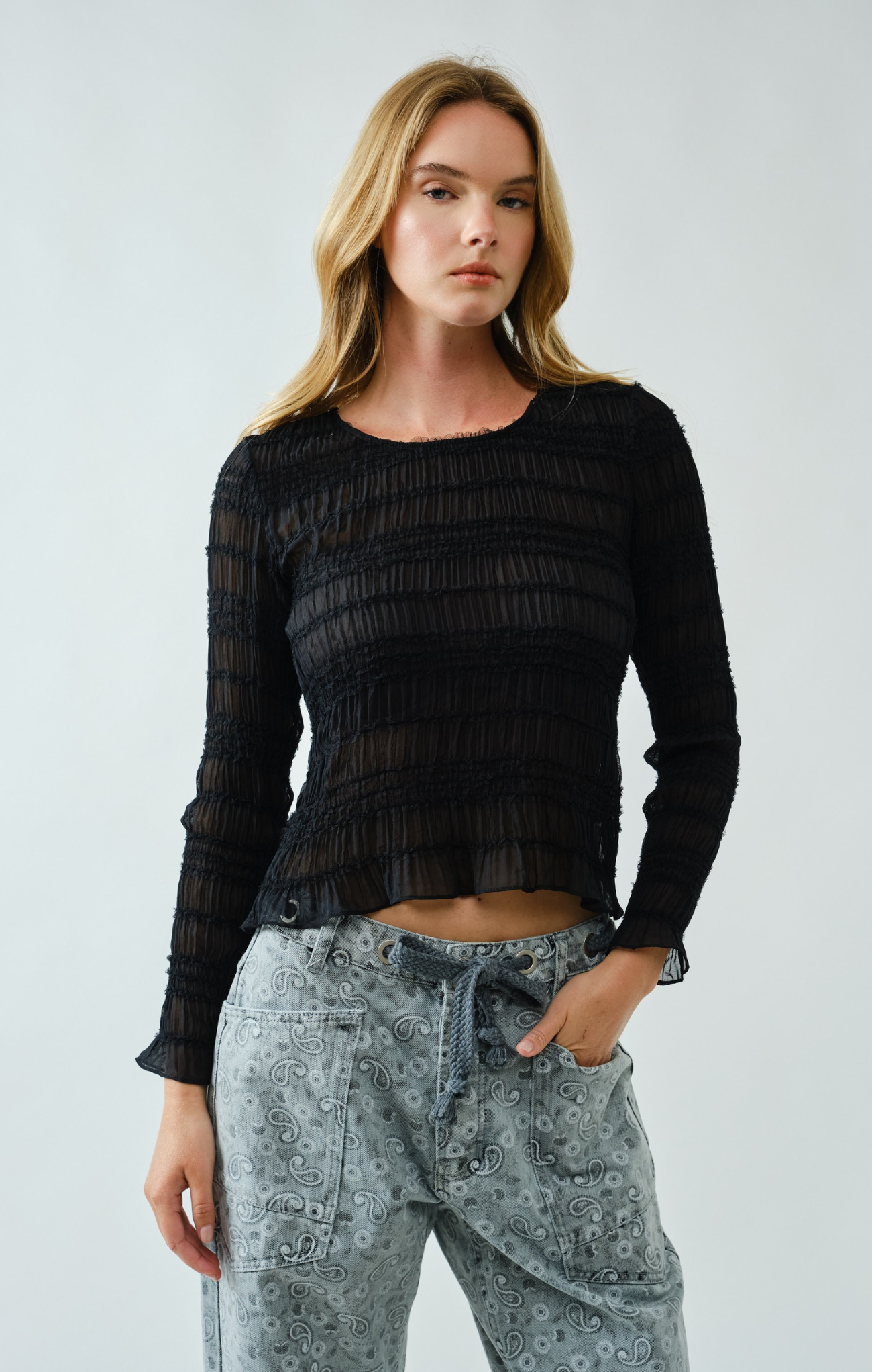 Woman wearing a black textured top and light blue jeans against a white background