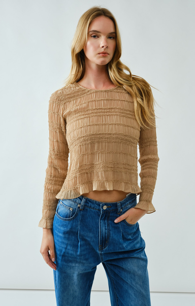 Woman wearing a beige textured top and blue jeans against a white background