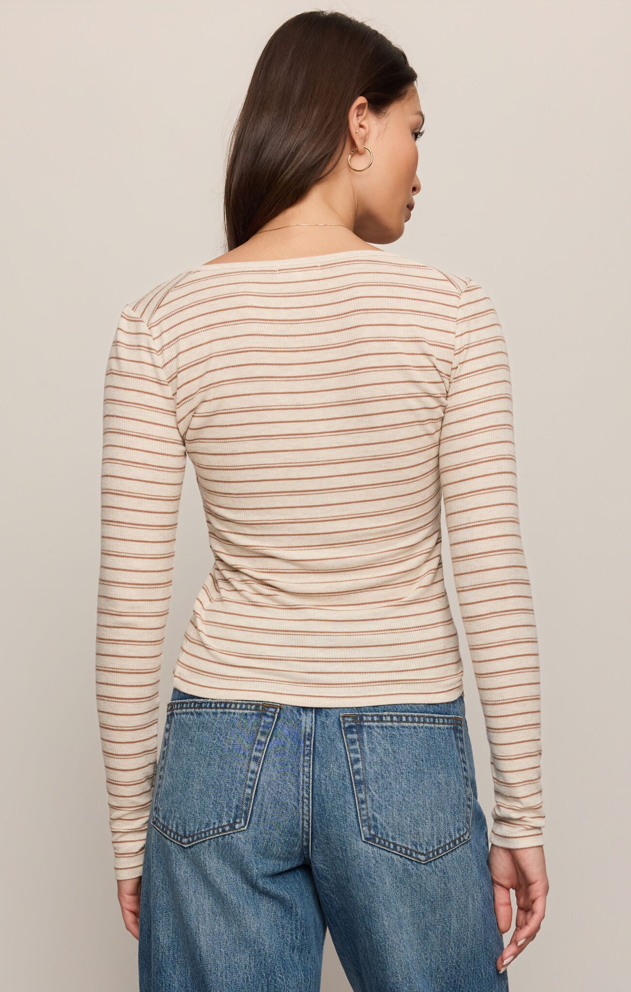 Woman wearing a striped long-sleeve top and blue jeans against a plain background