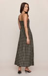 A woman modeling a sleeveless maxi dress with thin straps and a black and white windowpane plaid pattern, shown from a three-quarters back view against a solid light beige studio background.